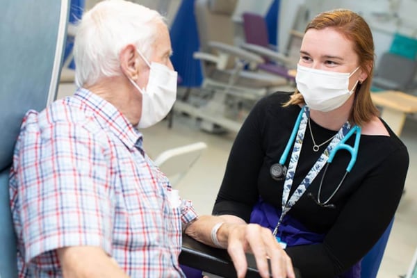 Consultant speaking with an elderly patient both wearing masks